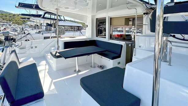 Convés de barco com área de estar, mesa e vista para outros barcos na marina.