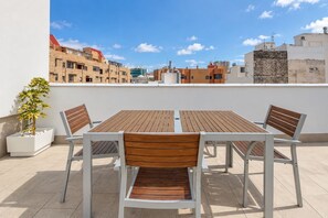 Terraço no telhado com mesa e cadeiras de madeira, um vaso de planta e vista para a cidade.