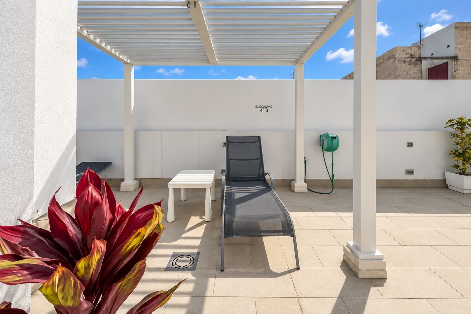 A covered outdoor area with a lounge chair, a table, and a potted plant.