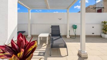 A covered outdoor area with a lounge chair, a table, and a potted plant.