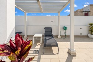 A covered outdoor area with a lounge chair, a table, and a potted plant. - GuestReady - 04B Livian Suites Terraza Ext 4 pax (Las Palmas de Gran Canaria)