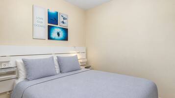 A bedroom with a bed, a headboard, and wall art depicting ocean scenes.