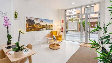 A hotel lobby with a reception desk, seating area, a large cityscape painting, and a view through the glass doors.