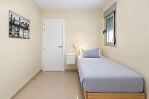 A bedroom with a bed, a bedside table, a nightstand, a wall-mounted lamp, a door, and a window. - GuestReady - 04B Livian Suites Terraza Ext 4 pax (Las Palmas de Gran Canaria)