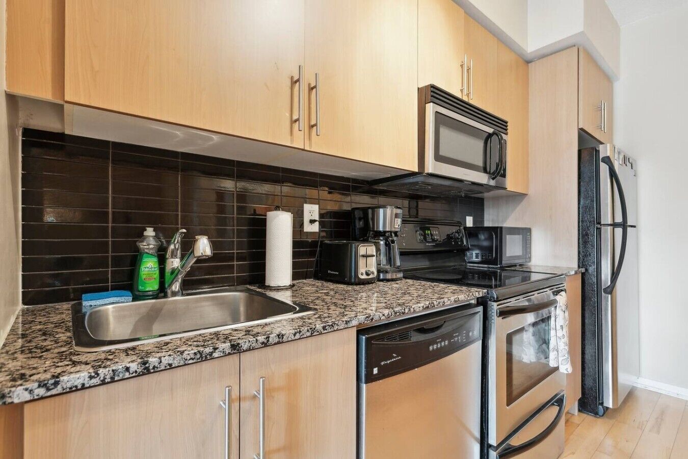 A modern kitchen with wooden cabinets, a granite countertop, a microwave, a toaster, and a dishwasher.