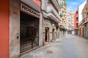 A narrow street with a building labeled 'ROSAMAR' on the left, featuring a large metal gate and a small entrance. - GuestReady - Rosamar 105 M (Las Palmas de Gran Canaria)
