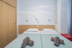 A hotel room with two beds, a wooden wardrobe, a red nightstand, and a wall-mounted phone. - GuestReady - Rosamar 105 M (Las Palmas de Gran Canaria)
