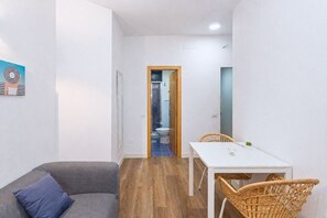 A small, modern room with a sofa, a dining table, and a chair. There is a door leading to a bathroom with a toilet and a shower. - GuestReady - Rosamar 105 M (Las Palmas de Gran Canaria)