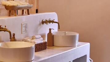 A bathroom with a white sink, a wooden door, a window, and shelves with toiletries.