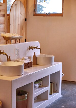 A bathroom with a white sink, a wooden door, a window, and shelves with toiletries.
