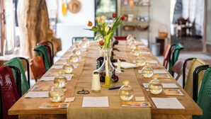 A long wooden table with a vase of flowers, candles, and glass bottles, surrounded by chairs.
