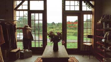 Une pièce avec une grande fenêtre, une table sur laquelle se trouve un vase, une chaise et un portant à vêtements.