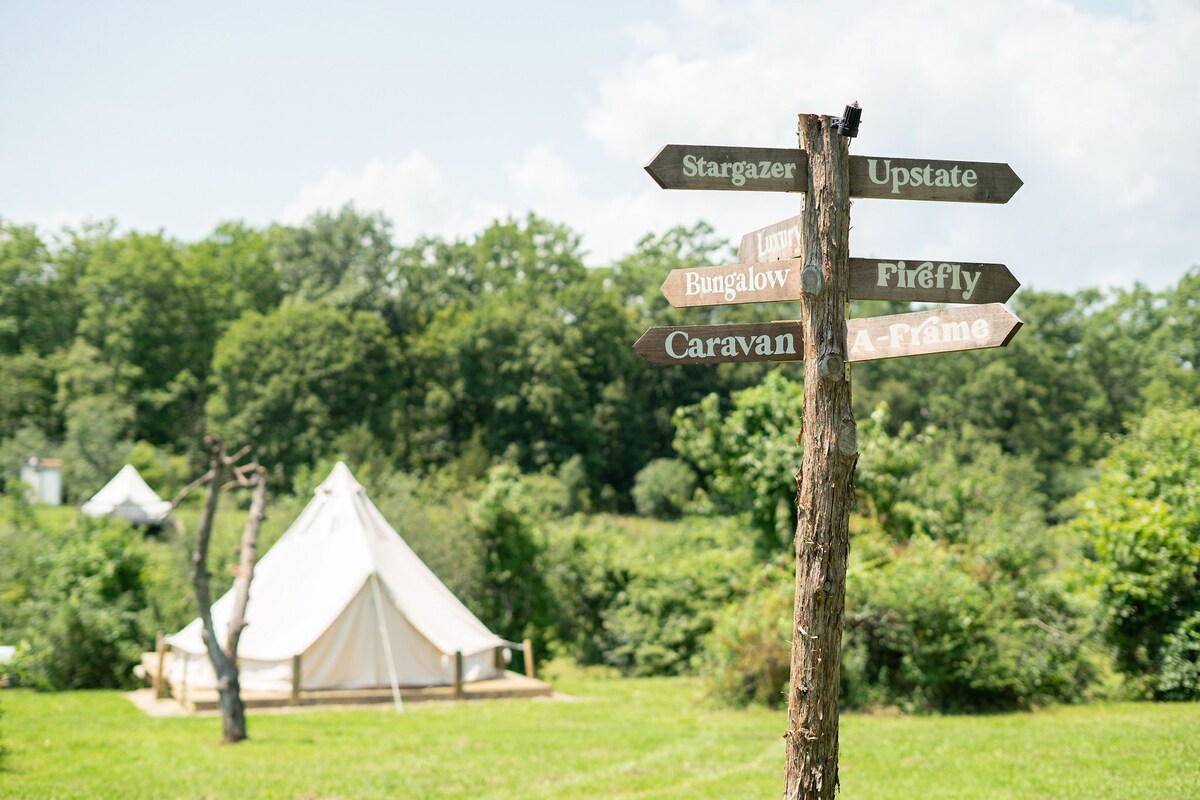 A wooden signpost with directions to various accommodations including Stargazer, Upstate, Bungalow, Firefly, Caravan, and A-Frame.