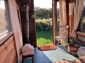 A wooden room with a view of a grassy area, a small stool, a fan, and a table with a mat.