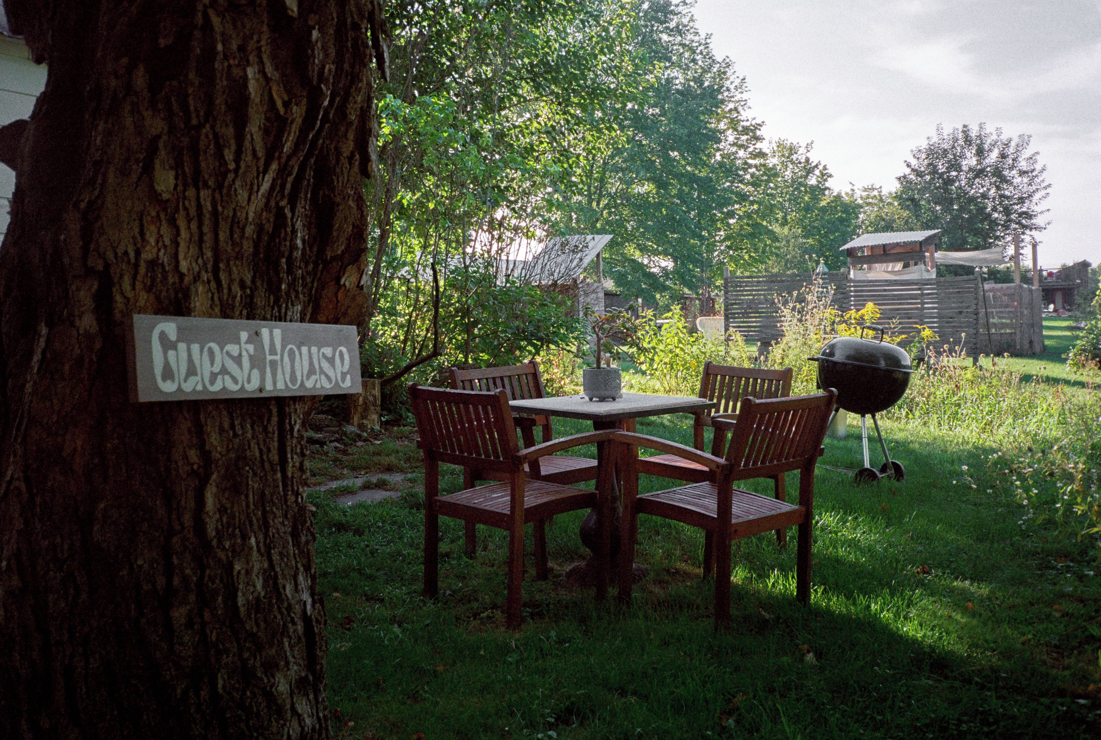 A wooden table and chairs set outdoors with a sign reading 'Guest House' on a tree trunk.
