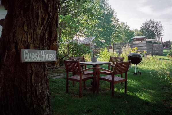 A wooden table and chairs set outdoors with a sign reading 'Guest House' on a tree trunk. - Gatherwild Ranch (Germantown)