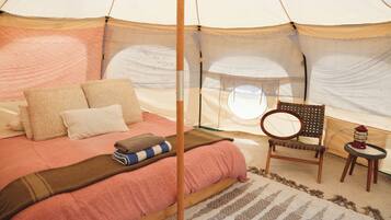 A tented room with a bed, pillows, a chair, a small table, and a lantern.