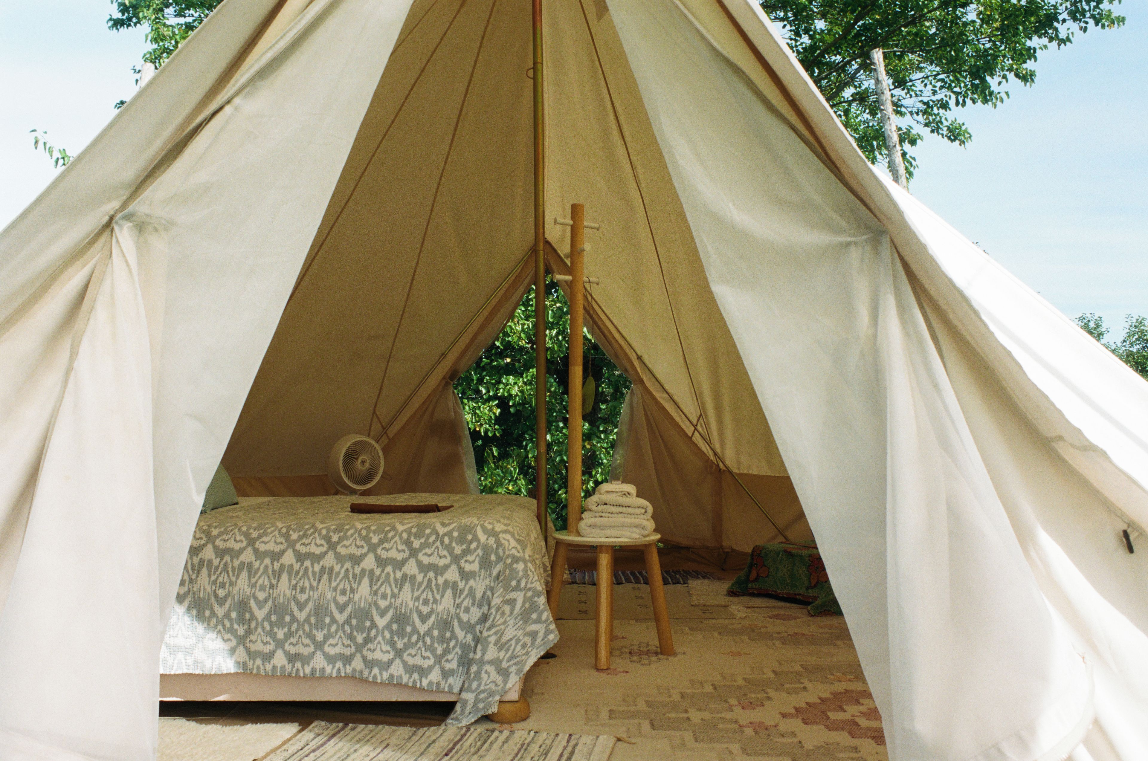 A tent with a bed, a fan, and a stack of towels.