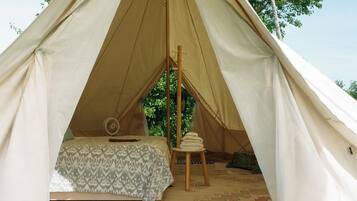 A tent with a bed, a fan, and a stack of towels.