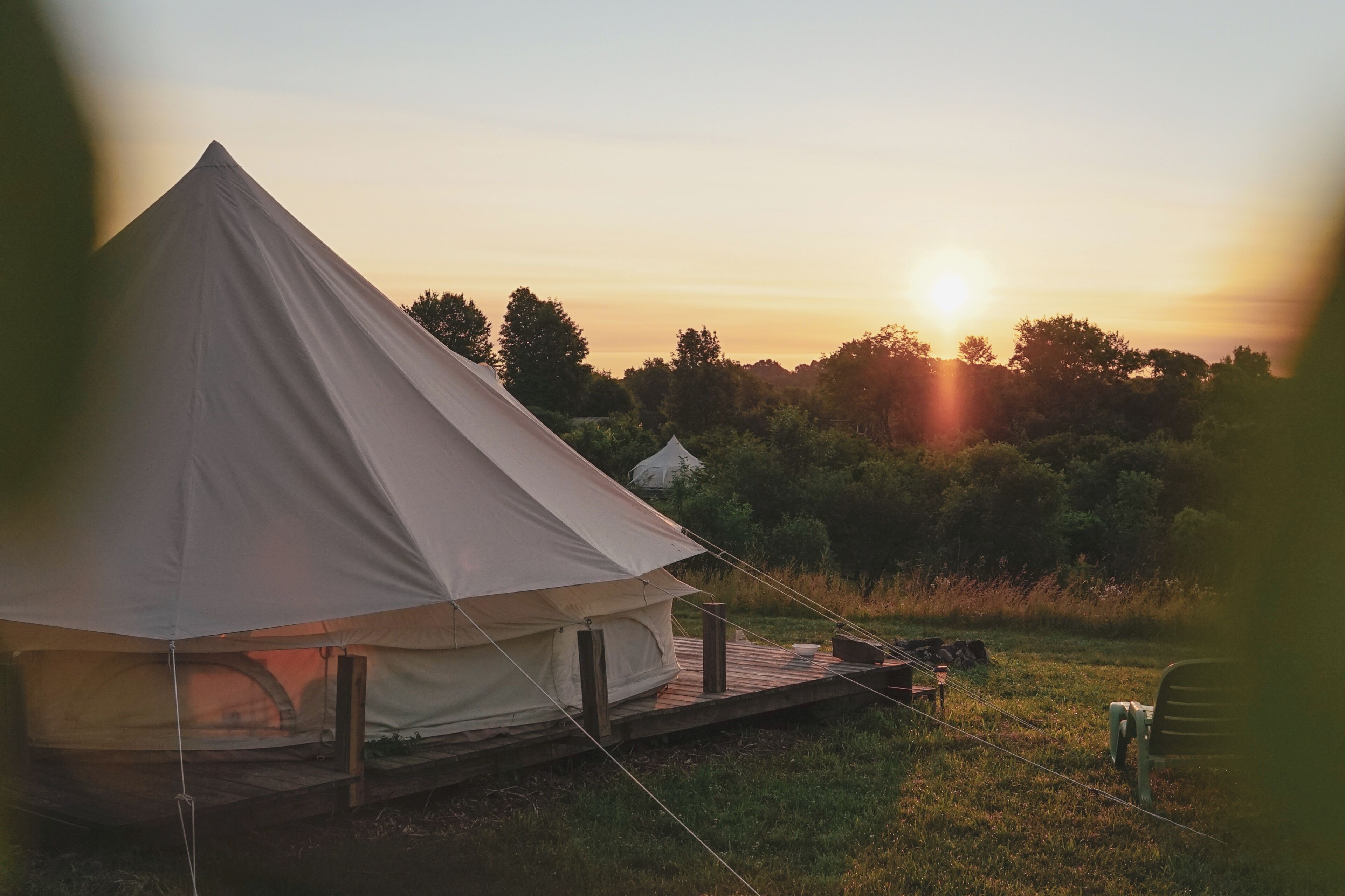 A large tent with a platform, surrounded by a grassy field and trees, during sunset.
