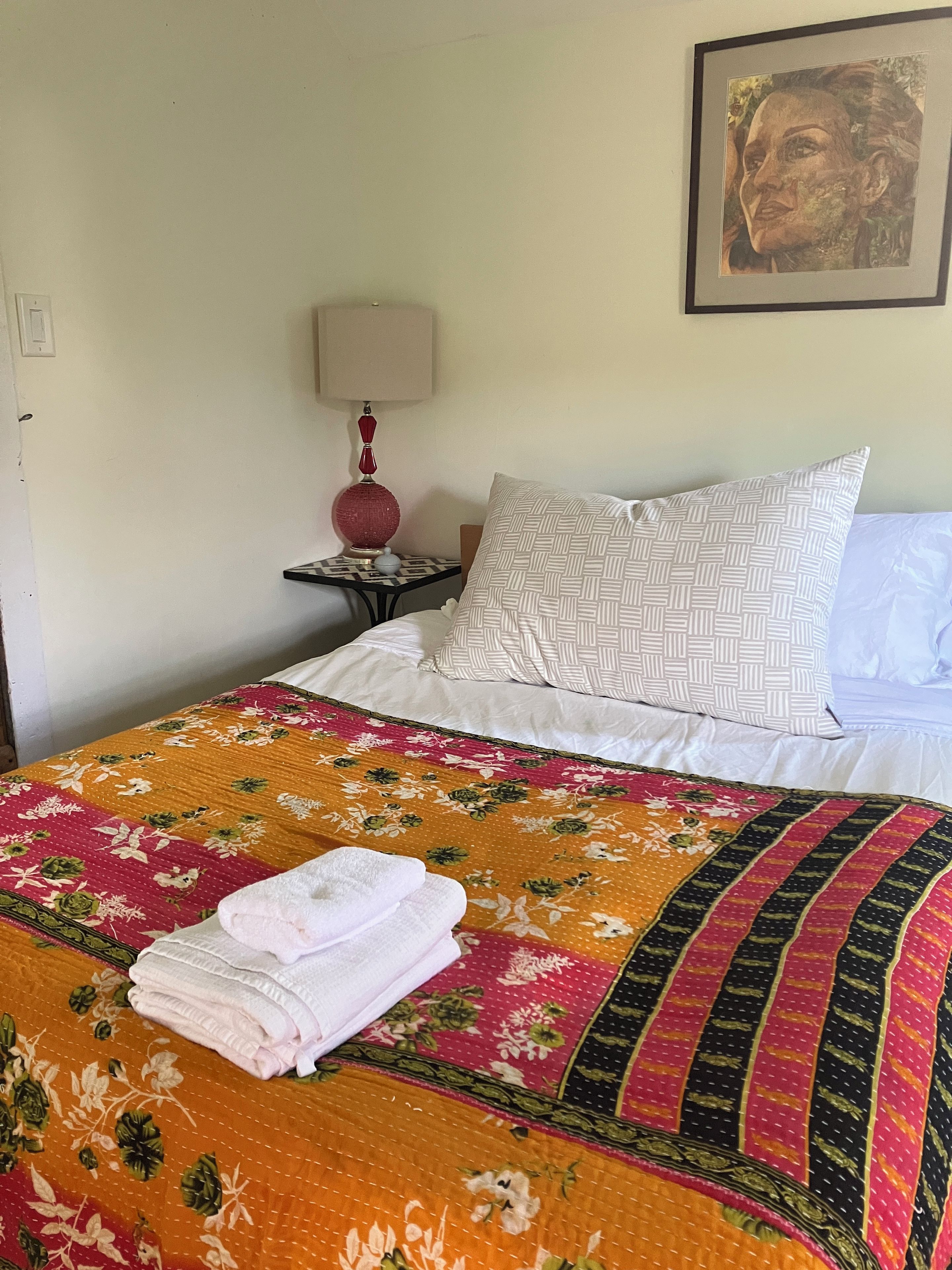 Un lit bien fait, avec une courtepointe à motifs floraux, un coussin à dessins et une serviette pliée posée sur le lit.