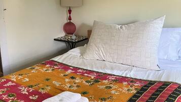 Un lit bien fait, avec une courtepointe à motifs floraux, un coussin à dessins et une serviette pliée posée sur le lit.