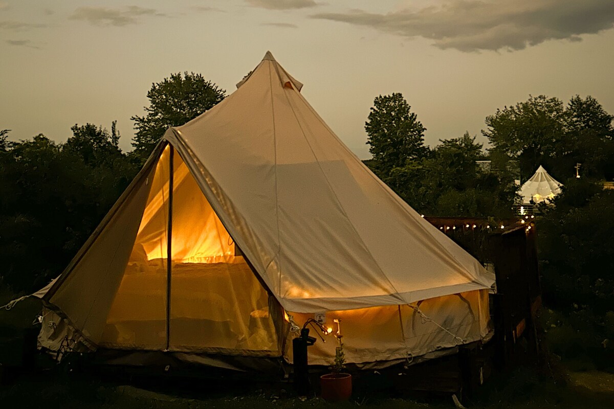A large, white tent with a triangular entrance, surrounded by trees and a cloudy sky.