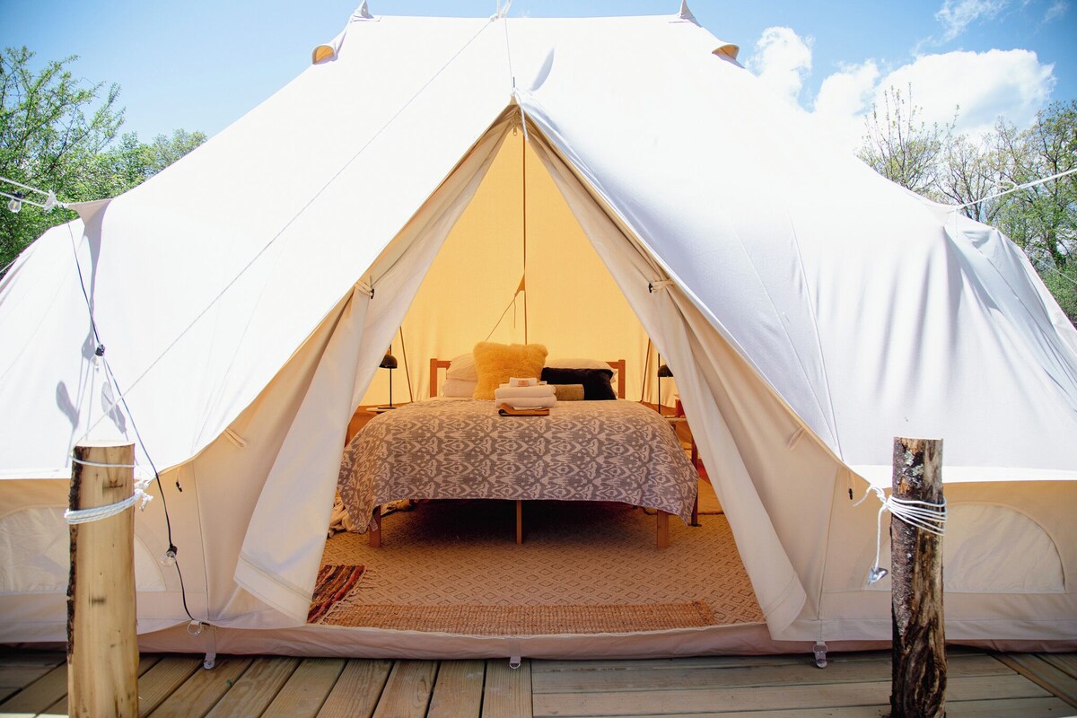 A tent with a bed inside, ropes securing it, and a wooden deck outside.