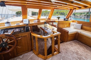 A boat's interior with a wooden helm station, a control panel, a dining area, and a seating area with a view of the water. - Sun-Kissed Sailing Adventure in Split, Croatia (Split)