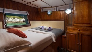 Uma cabana com uma cama, uma janela com vista para o mar, um espelho redondo pequeno e armários de madeira.