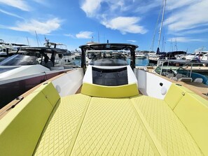 Interior d'una embarcació amb sòl groc, zona d'habitacle i vista de d'altres vaixells al port esportiu.
