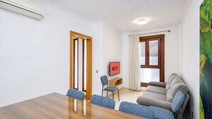 Ein Hotelzimmer mit einem Holztisch, zwei blauen Stühlen, einem grauen Sofa, einem Bild an der Wand und einem Schild mit der Aufschrift 'GUEST READY'.