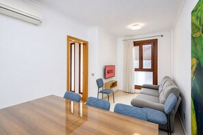 Ein Hotelzimmer mit einem Holztisch, zwei blauen Stühlen, einem grauen Sofa, einem Bild an der Wand und einem Schild mit der Aufschrift 'GUEST READY'.
