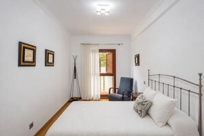 Een slaapkamer met een bed, een stoel, een vloerlamp en twee foto's in lijsten aan de muur.