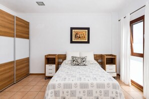 A bedroom with a bed, nightstands, a wardrobe, a picture on the wall, and a window with curtains. - GuestReady - Naranjo Duplex Central Place (Telde)