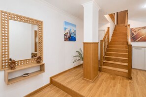 Eine Treppe mit Holzboden und Geländer, die zu einer Zwischenebene mit einem Holzschrank und einem Spiegel mit Zierrahmen führt.