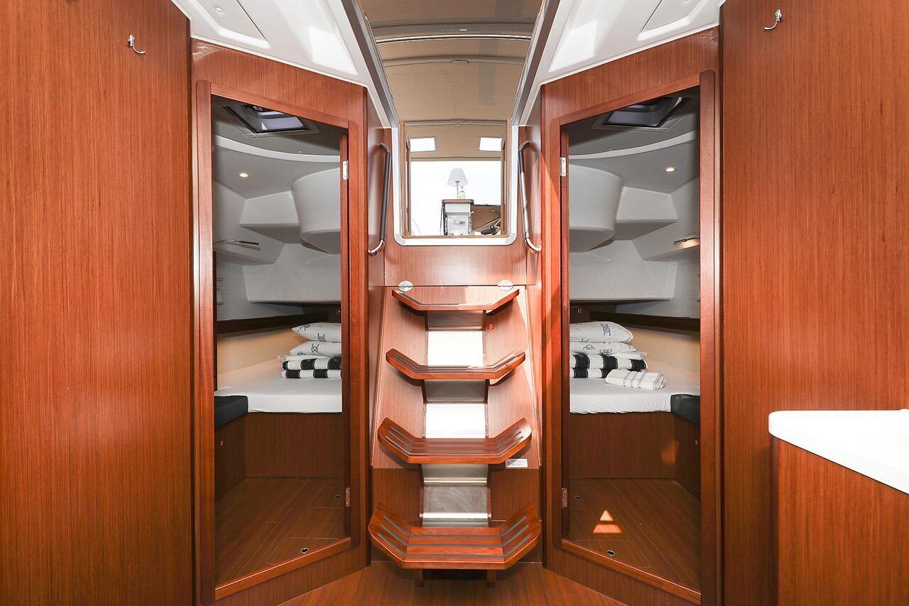 A narrow, wooden-lined corridor with a central staircase leading to a small room with a bed and a window.