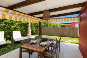 An outdoor patio with a wooden table set for dining, surrounded by chairs, and a covered area with striped awnings. - GuestReady - Los Tunos BBQ Garden (San Bartolomé de Tirajana)