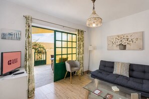 A living room with a sofa, a glass coffee table, a TV, and a painting. - GuestReady - Cosy Bungalow with Pool and Terrace (Costa Calma)