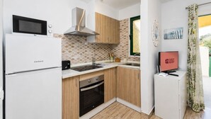 Et kompakt køkken med mikrobølgeovn, komfur og vask. Der er et lille køleskab og et fjernsyn på et stativ. Køkkenet har træskabe og en mønstret backsplash.