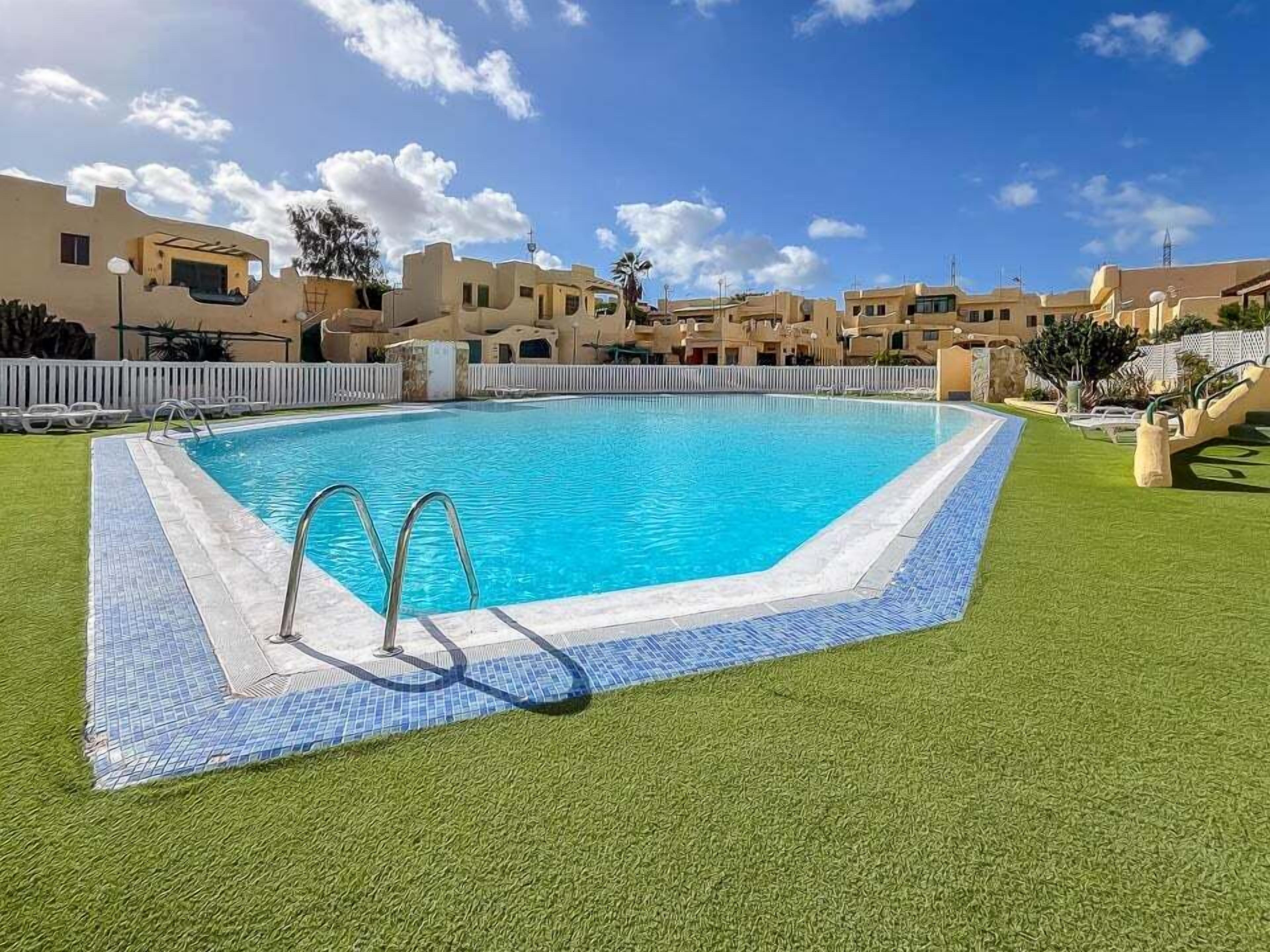 Una piscina amb vora de rajola, envoltada d'herba artificial i una tanca blanca.
