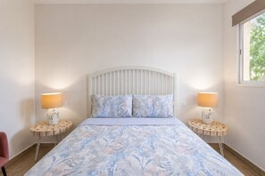 A bedroom with a bed, two bedside lamps, a window, and a chair. - GuestReady - Cosy Bungalow with Pool and Terrace (Costa Calma)