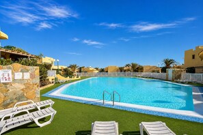 A swimming pool with a stone wall and a white fence, surrounded by greenery and buildings. - GuestReady - Cosy Bungalow with Pool and Terrace (Costa Calma)
