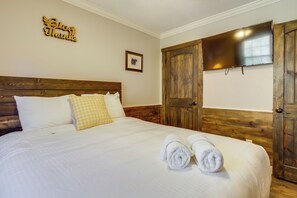 A neatly made bed with white and yellow pillows, a framed picture on the wall, and a wooden wardrobe with a TV mounted above it. - Pigeon Forge Cabin w/ Swim Spa: Walk to Dollywood! (Pigeon Forge)