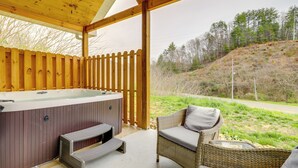 A wooden deck with a hot tub, wicker furniture, and a view of a hilly landscape. - Dolly's Cabin: Private Hot Tub, Walk to Dollywood (Pigeon Forge)