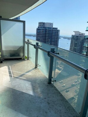 Ein Balkon mit Glastür, Metallgeländern und Blick auf hohe Gebäude sowie Wasser.