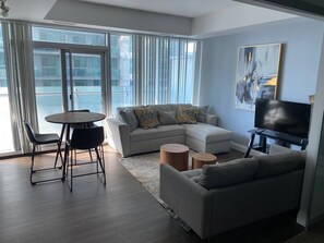 Ein modernes Wohnzimmer mit einem Ecksofa, einem runden Esstisch und einem Flachbildfernseher.