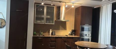 Cocina compacta con comedor, electrodomésticos integrados y un amplio ventanal.