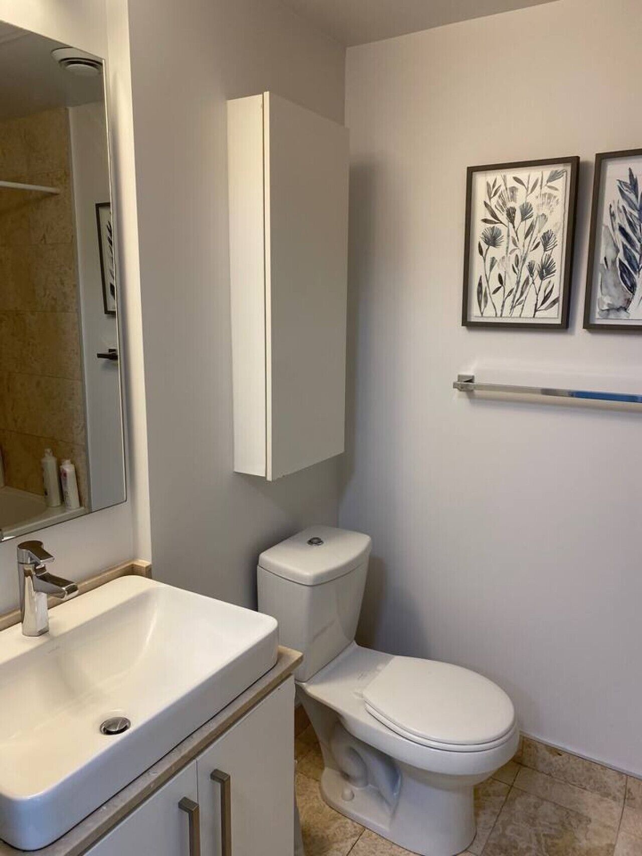 Une salle de bain avec un lavabo blanc, des toilettes, un miroir et deux œuvres d’art encadrées accrochées au mur.