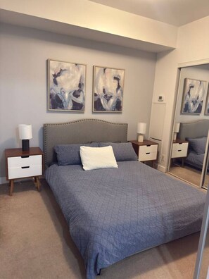 Ein Schlafzimmer mit einem Bett, zwei Nachttischen, einem Spiegel und abstrakter Wandgestaltung.